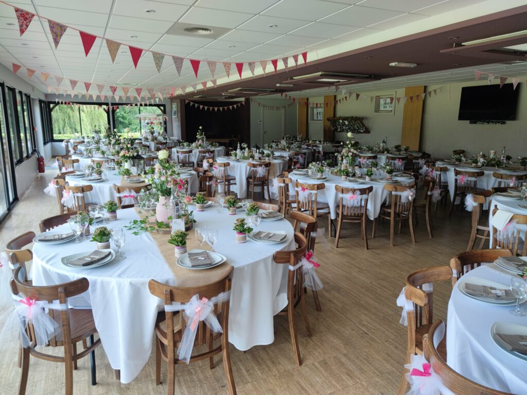 La salle décorée pour un mariage : tables rondes, fanions et chaises nouées de tulle rose